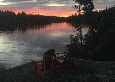muskoka chairs on river at sunset